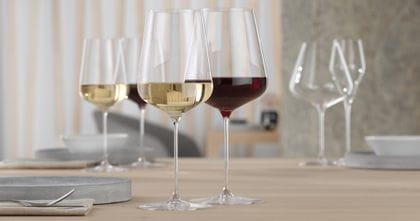 Ein mit Rotwein gefülltes SPIEGELAU Definition Bordeauxglas und ein mit Weißwein gefülltes SPIEGELAU Definition Weißweinglas stehen auf einem Tisch. Im Hintergrund stehen wieder die gleichen gefüllten Weingläser.<br/>