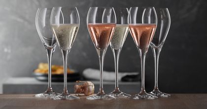 Eine Gruppe von SPIEGELAU Party Champagnergläsern. Zwei davon sind mit Rosé-Champagner gefüllt, zwei mit normalem Champagner und zwei sind leer. Ein Korken liegt auf dem Tisch.<br/>